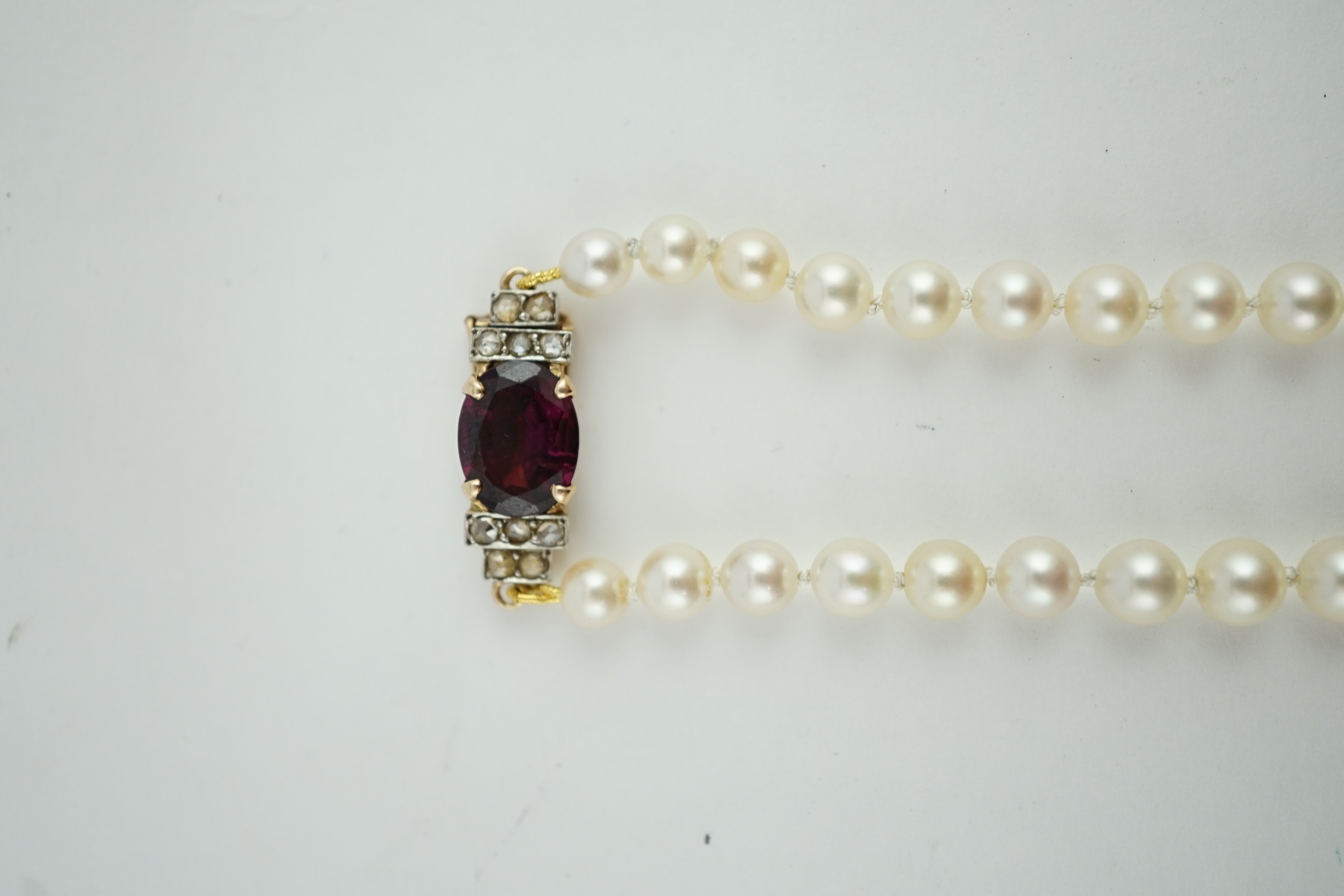 A single strand graduated cultured pearl necklace, with a gold, garnet and rose cut diamond cluster set clasp